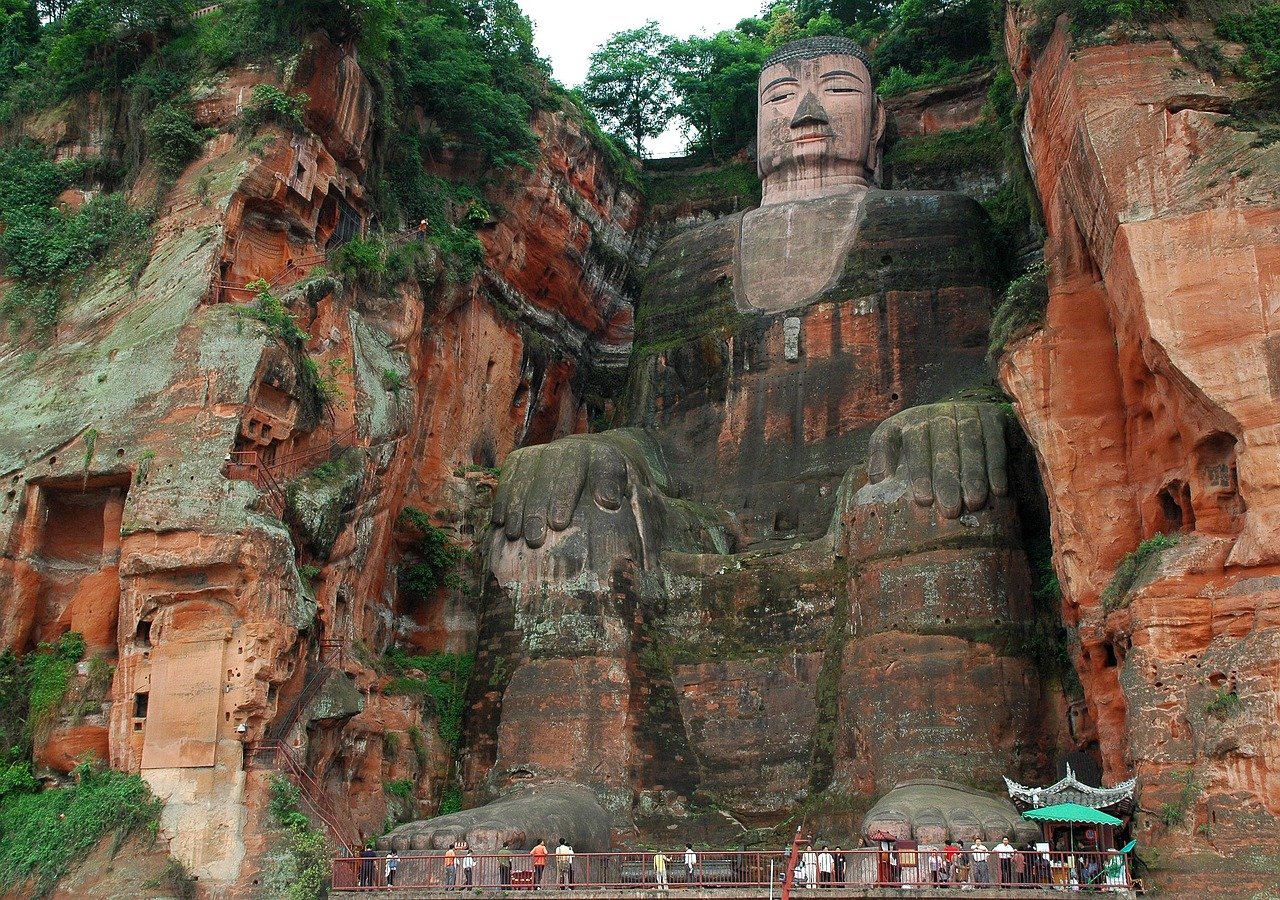 The complete seated Leshan Giant Buddha, with visitors at its feet showing its immense scale.