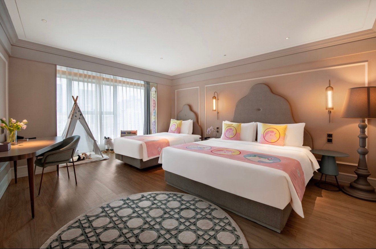 Hotel room with a king-size bed against an orange feature wall and a bathroom behind glass.